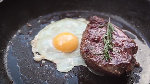 Delicious steak with egg and rosemary cooking on pan.