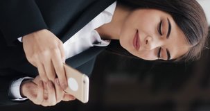 Vertical video. Young beautiful business woman using smartphone. She Surfing the Internet. Concept: new business, communication, banker, call. Vertical frame for mobile devices