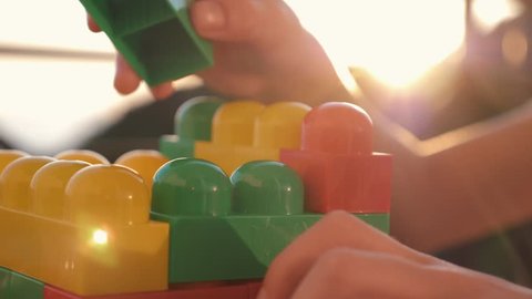 Close-up of the boy's hand collecting the developing designer of the lego sitting at the table in the rays of the setting sun. The concept of a happy childhood