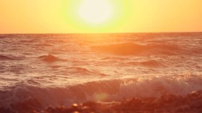 Big waves on a sea beach at sunset. Beautiful waves of slow motion video on the background of the orange sun