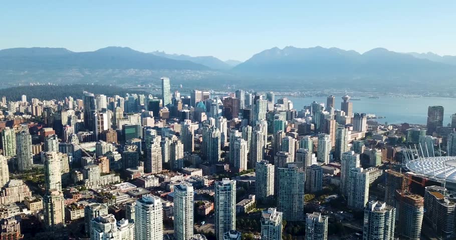 Aerial flight overlooking downtown Vancouver skyline with mountains and blue sky