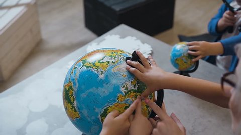 Top view. A blonde woman discussing over a globe with the kids at indoors. Teacher with pupils who discussing over a globe at on geography lesson at school, slow motion
