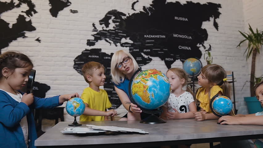 Teacher assisting school kids in reading globe in geography classroom at elementary school. An attractive teacher are educating of his pupils at elementary school and using a globe to teach them about Royalty-Free Stock Footage #1014720179