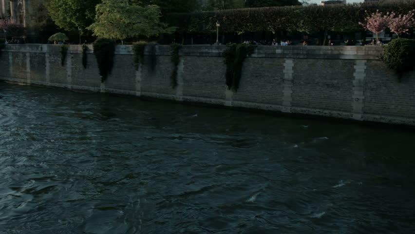 Camera panning left following the Seine River tilt up to reveal side rear of Notre Dame Cathedral in Paris, France
