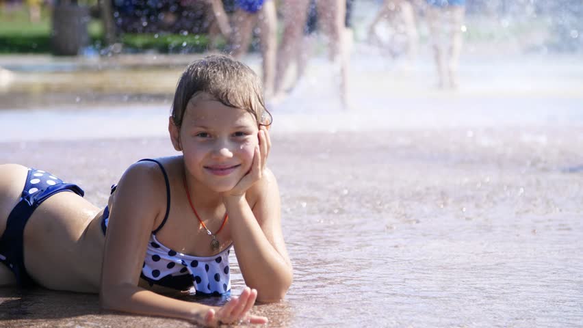 Smiling, happy eight year old girl in swimsuit having fun in splashes in st...