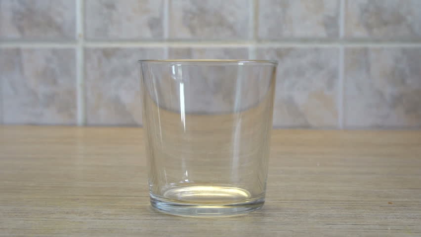Transparent glass Cup. Water pours from above. Kitchen interior. Light background. Wooden table. Square tiles on the wall. Quenching thirst. Royalty-Free Stock Footage #1014739106