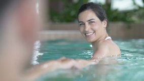 Portrait of brunette woman in spa pool pulling on man's arm