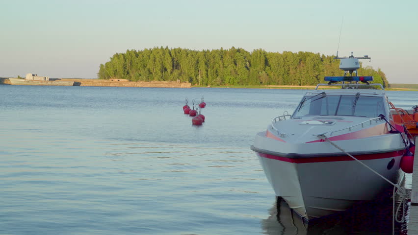 A white speedboat docking on the port in Tallinn Estonia with the green trees on one island on the back