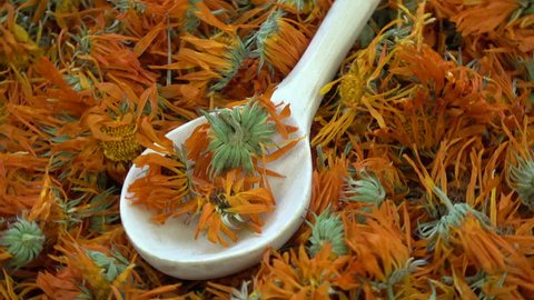 Rotating dried marigold calendula medical flowers background with wooden spoon