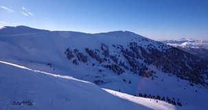 Aerial drone video of snow north face ridge with ski center reveal and sun shining in the background