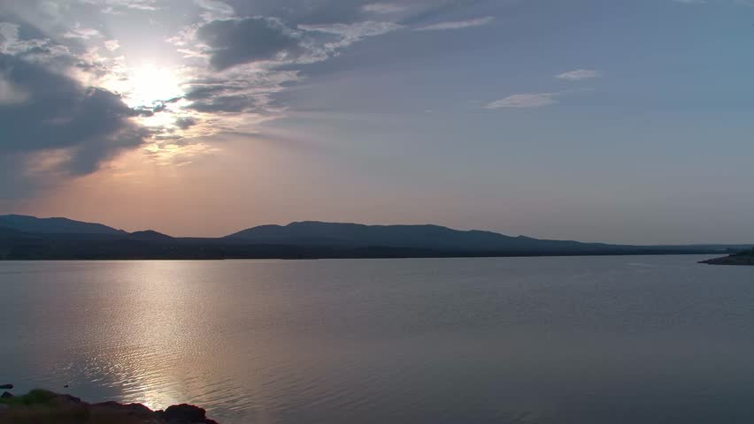 Sunset with clouds view from La Mine in Leucate, Langdoc Rousillon region of South of France. Beautiful blue lake in the foreground with mountains in the background. Slow pan right.