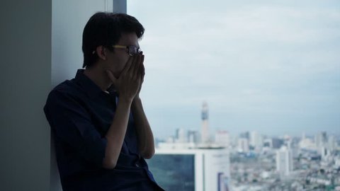 PTSD Mental health concept, Young depressed be tired  asian man massaging his nose and keeping eyes closed while sitting alone near window in evening time.
