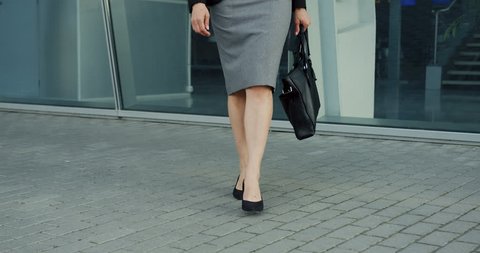 Caucasian woman legs in the business skirt and clothes on the heels walking out the office center on the street.