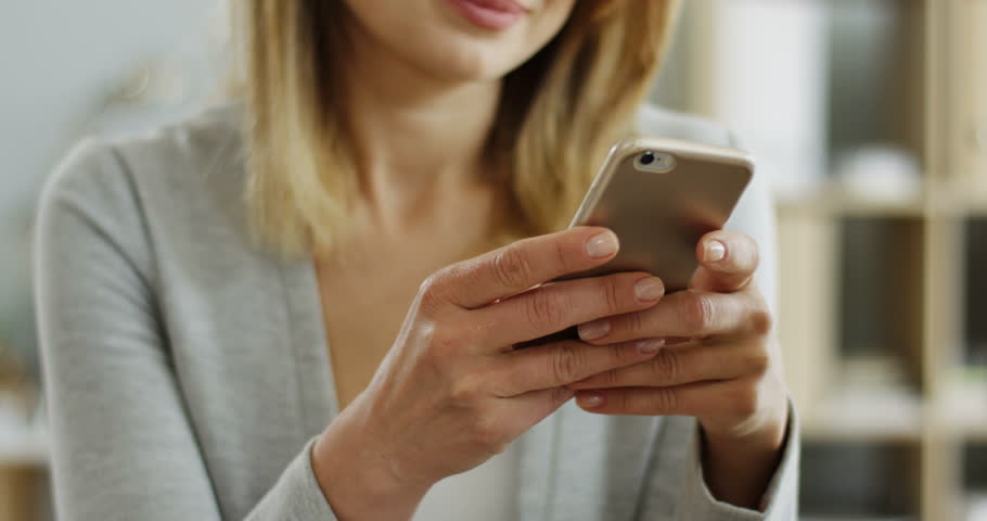 Close up of the pretty smiled woman in glasses texting while chatting on her smartphone device and making surprised face.