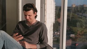 Man is watching a video on mobile phone, sitting on the balcony in sunset.