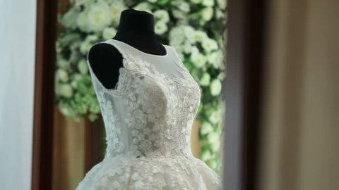 Beautiful white wedding dress is hanging on a hanger in a bedroom, slow motion shot, wedding day