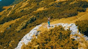 Aerial View Running woman on the top of mountain. Runner is jogging in summer sunny day around trees and mountains background under sun light with blue sky, Drone 4K Video
