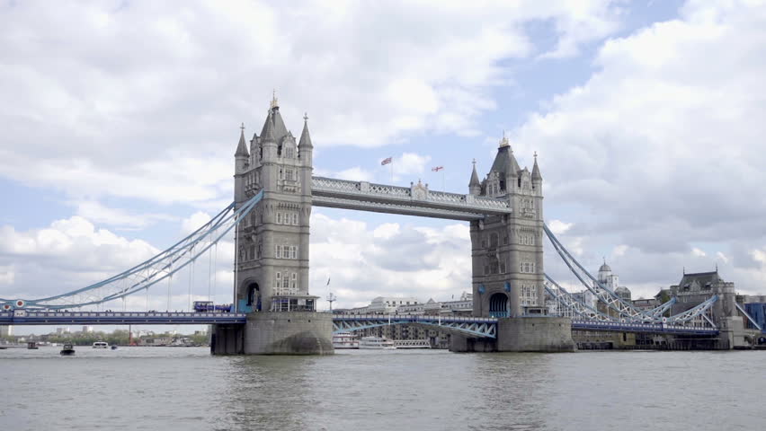 flags waving on Tower Bridge on The River Thames - cars and red bus driving across in London England UK