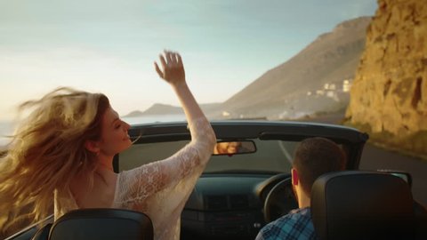 Couple exploring traveling with convertible driving along the ocean, woman happy in love with arms out the car