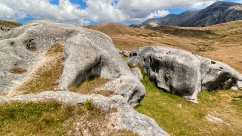HDR Timelapse/Hyperlapse of New Zealand grasslands showing rock formations made famous in Hollywood blockbusters.  Features slow panning motion with cloud motion set against a bright blue sky.
