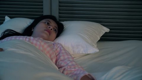 A lonely Asian woman can't fall asleep during the night. She is thinking something unhappy upset and important. She turns and toss but not help to sleep.