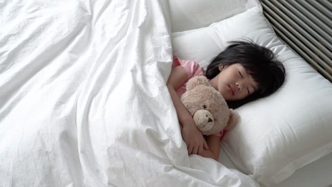 Asian adorable girl sleeps quietly and holding her cute fluffy teddy bear.