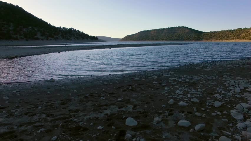 Dolly right type drone shot across the stony shore of a Colorado Rocky Mountain Lake, revealing a beached fishing kayak.