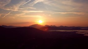 Video from above, aerial view of an amazing sunset behind some hills and a coast bathed by the Mediterranean Sea in Sardinia, Italy.