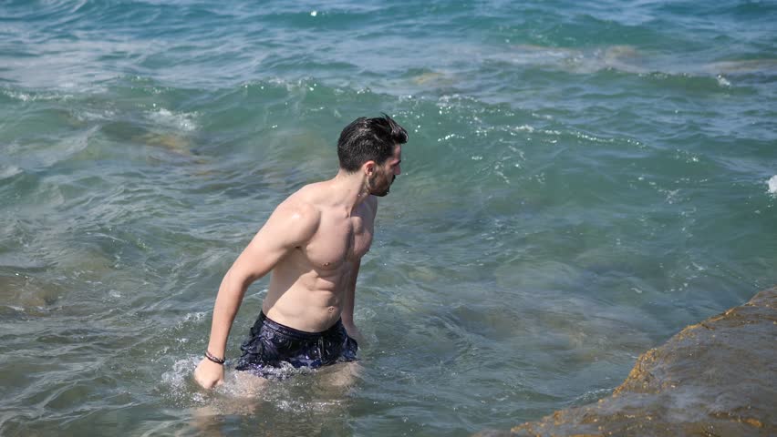 Handsome muscular young man standing in the sea by the coast and the beach
