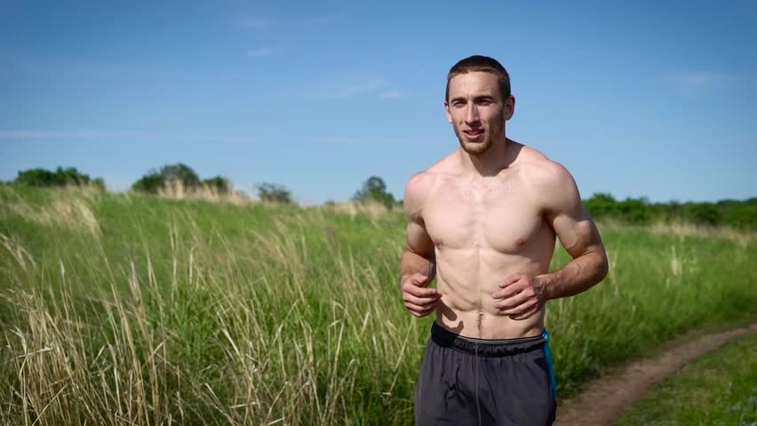Portrait of a muscular shirtless man running across the field.