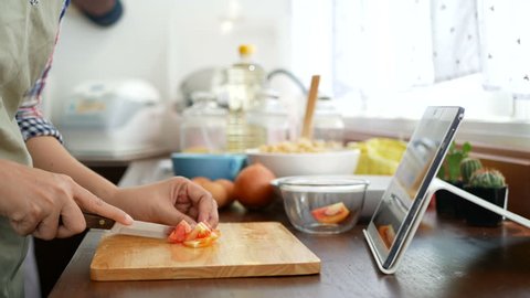 4K. woman slicing red tomato prepare ingredients for cooking follow cooking online video clip on website via tablet. cooking content on internet technology for modern lifestyle