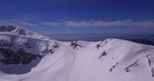 Aerial drone video side panning movement of rocky steep north faces in snow, with ridges and white peaks in the background