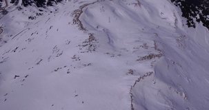 Aerial drone video side camera movement of off piste freeride route with ski tracks, rocky ridge and trees below