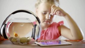 small female child is playing in a video game in tablet, sitting alone in room, headphones are on aquarium