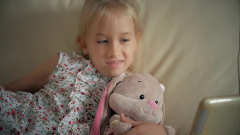 Cute girl and her favorite toy is a plush rabbit with tablet computer at home.