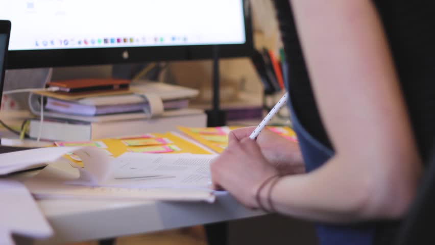 Woman writes notes with pencil on busy work desk as deadlines creep in | Shutterstock HD Video #1014817763
