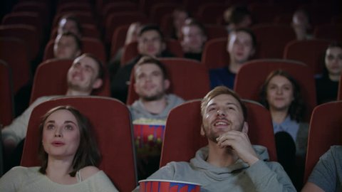 Young people laughing at cinema theater. Joyful people watching amusing comedy. Cheerful people smiling at movie theatre watching comedy film in slow motion. Friends spend weekend in cinema