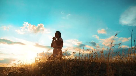 Girl folded her hands in prayer silhouette at sunset. woman lifestyle praying on her knees. slow motion video. Girl folded her hands in prayer pray to God. the girl praying asks forgiveness for sins