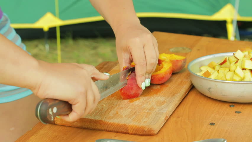 Young woman cuts a peach salad on a picnic with a knife.