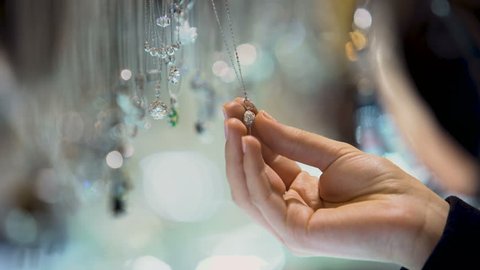 Female hand holding diamond pendant, jewelry assortment in luxury shopping mall