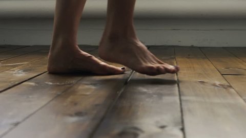 The girl is walking on the wooden floor. Female feet go on the wooden floor.