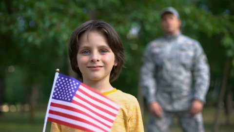 Adorable boy holding american flag, male soldier standing behind, safe future Stockvideó