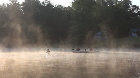 Fog drifting on a lake in the morning light with kids paddling in canoes.