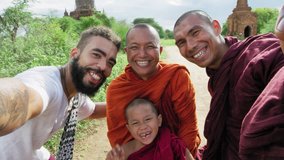 Authentic real monks and African American man tourist traveler in Bagan Mayanmar / Burma doing selfie picture or video with  smartphone, ancient pagoda view of Bagan.  Slow motion. 