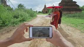 African American man tourist traveler taking photo or video with smart phone of Authentic real monks in Bagan Mayanmar / Burma walking with bamboo umbrellas. Slow motion pov hand held. 