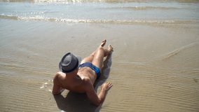 Summer lifestyle video of pretty young suntanned man in a hat. Enjoying life and sitting on the beach, time to travel. Looking at the sea