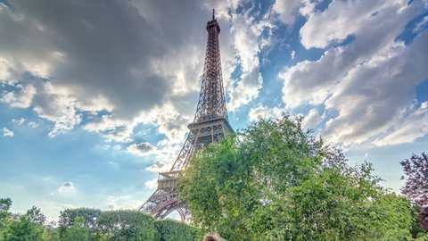 The Eiffel tower with warm rays of light in clouds during sunset timelapse hyperlapse. It is one of the most recognizable landmarks in the world. Blue cloudy sky at sunny evening