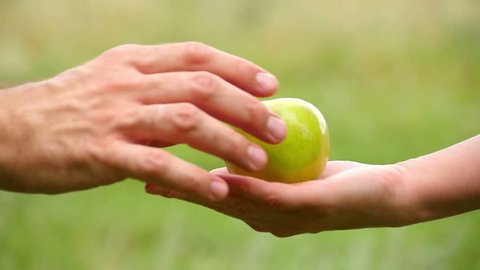 A man takes an Apple lying on a woman's hand. Exchange, kindness, care and love. The girl holds the Apple and gives it to the man.