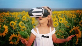Little girl in virtual reality goggles in the sunflower field on sunset. Child looking at virtual reality glasses at sun.