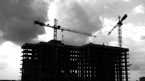 Black and white footage presents the time lapse of a construction site. It shows two huge cranes lifting construction materials. related to construction cranes, construction sites, real estate.